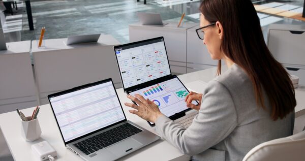 Fintech Specialist Examines Diverse Financial Dashboards On Multiple Laptop Displays